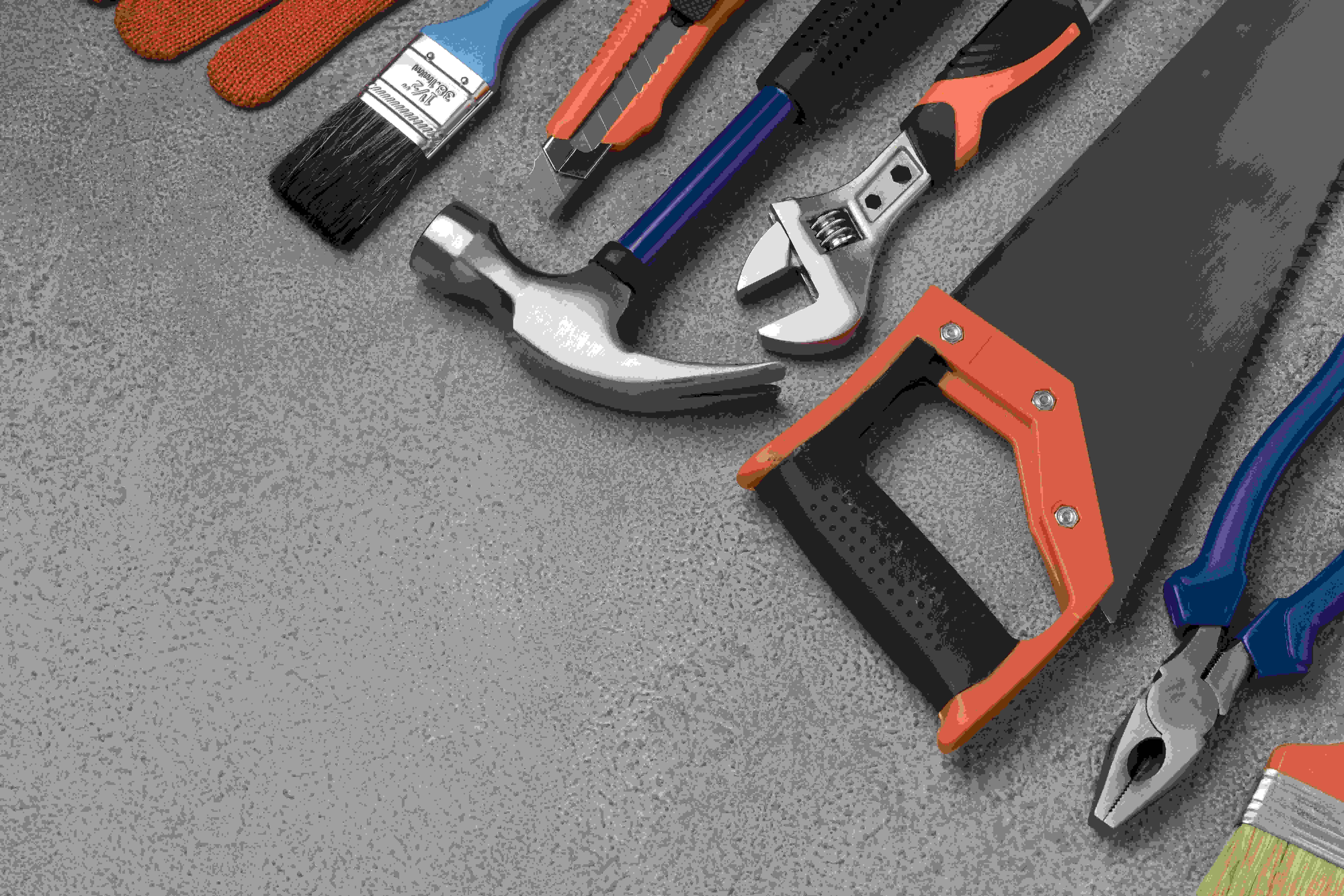 Verschiedene Handwerkzeuge wie Hammer, Säge, Schraubenschlüssel und Zange auf grauer Oberfläche.